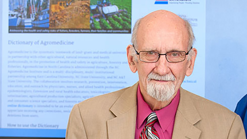 Photo of Ernest Hodgson in front of a screen about the agromedicine.