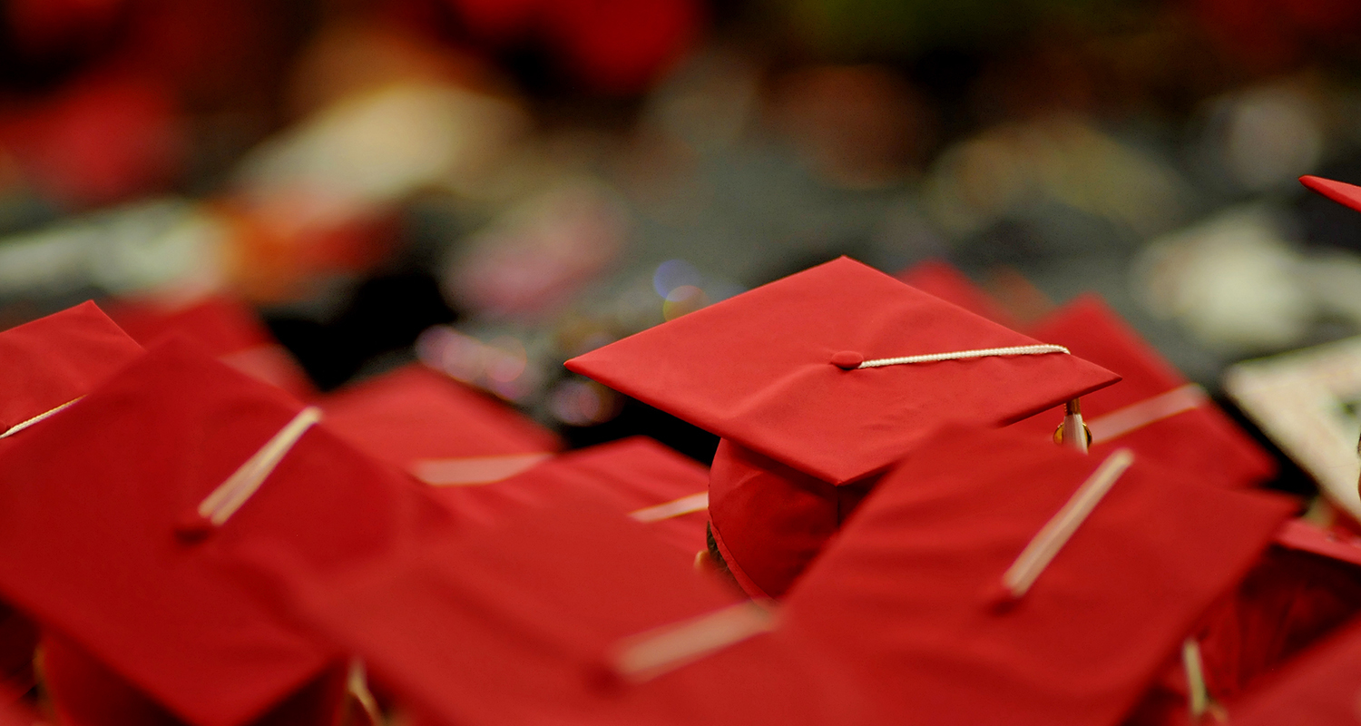 Red mortarboards viewed from above during graduation ceremony.