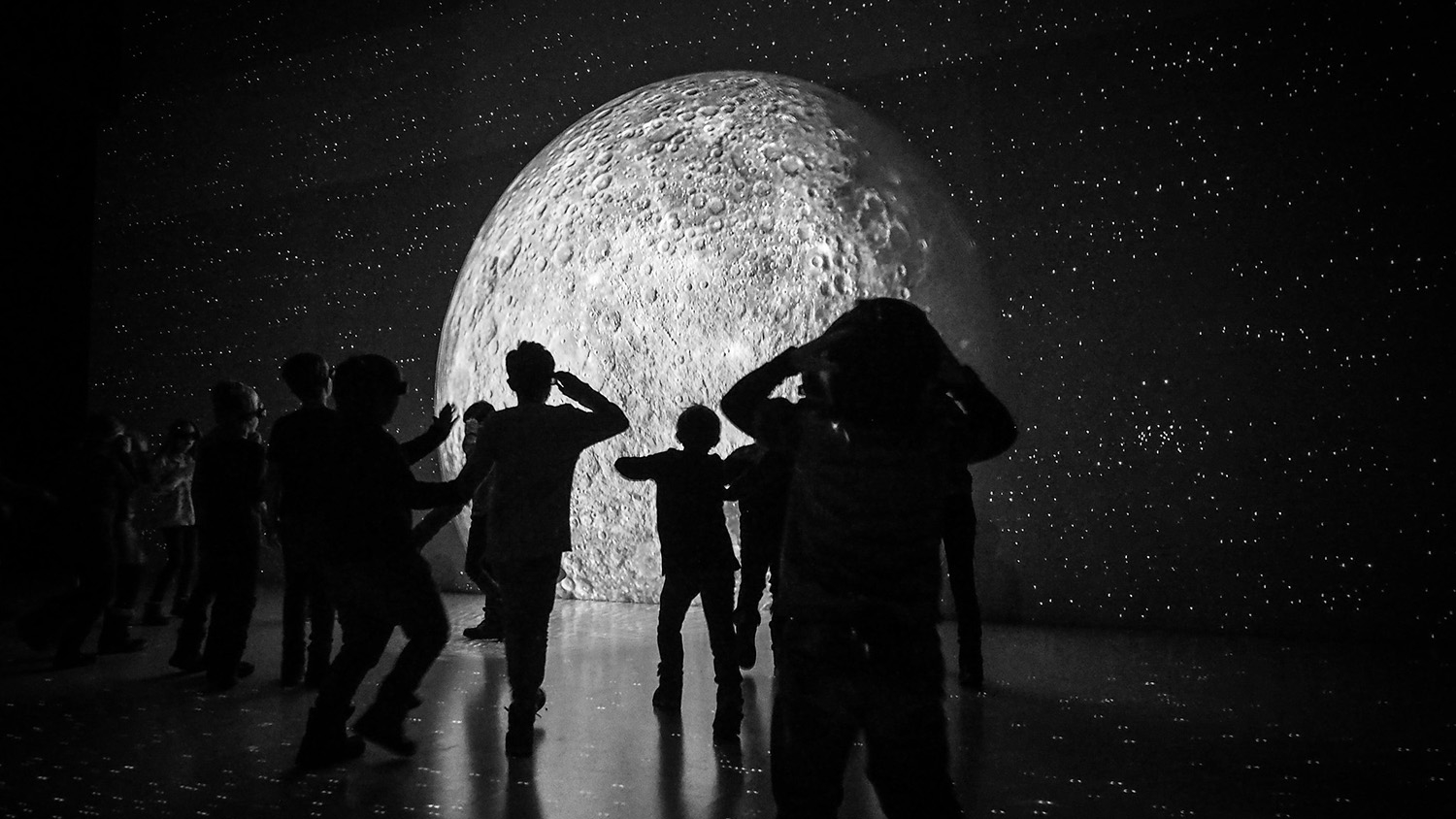 children silhouetted in front of a museum exhibit about the moon