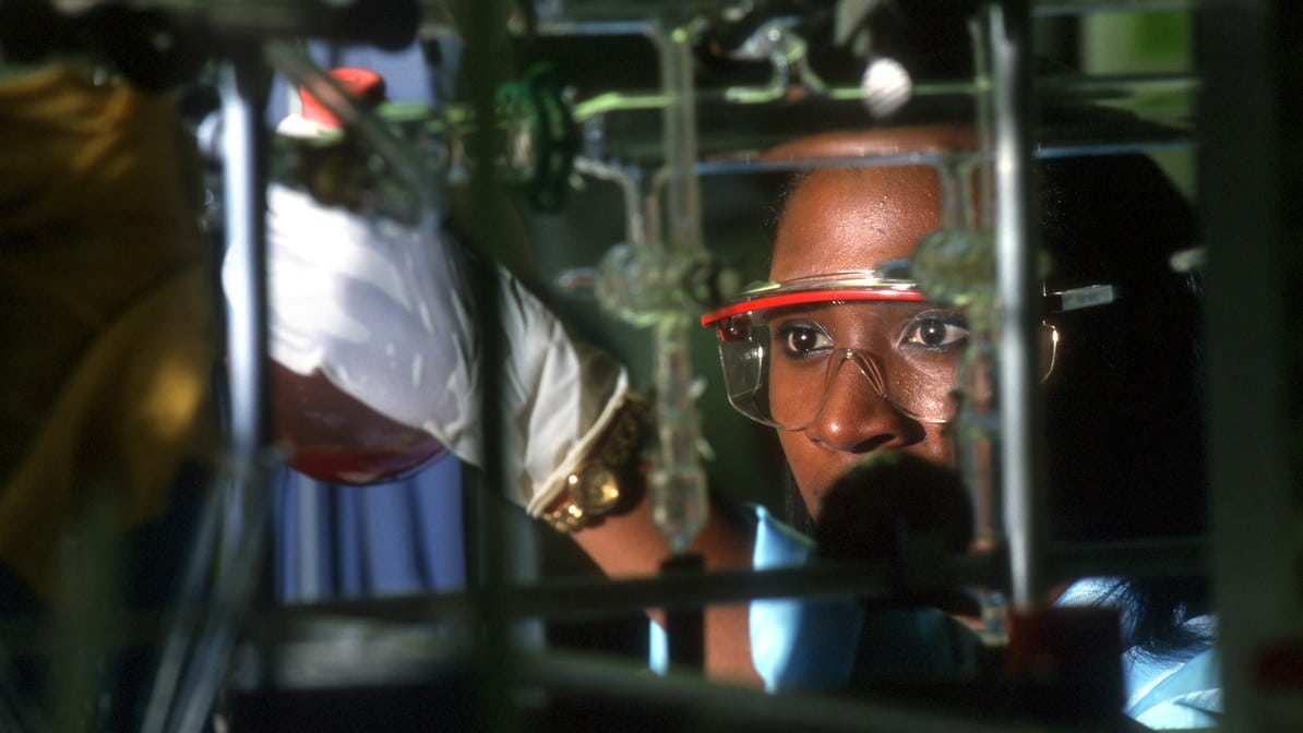 Researcher in lab goggles looking at a sample in a beaker