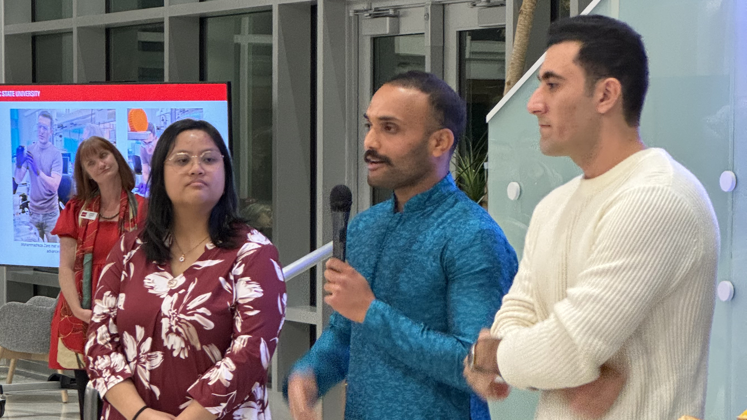 Four people standing in a building lobby, with one speaking into a microphone.